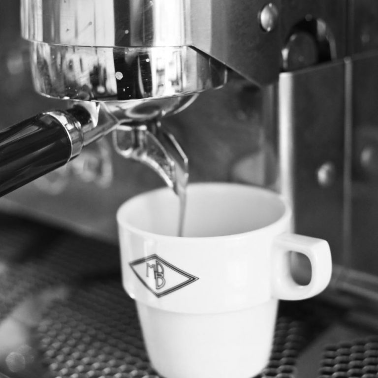 Een koffiemok met het meneerdeboer logo, die gevuld wordt met koffie.