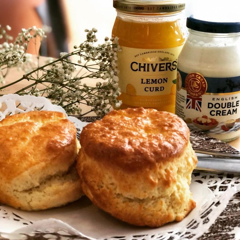 Scones met een potje clotted cream en een potje lemoncurd erachter.